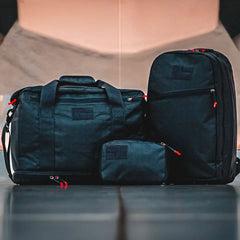 Three black Kit Bag x Carryology - Ultra Blaze travel bags with red zipper pulls are lined up on a flat surface, each made from durable UHMWPE fabric.