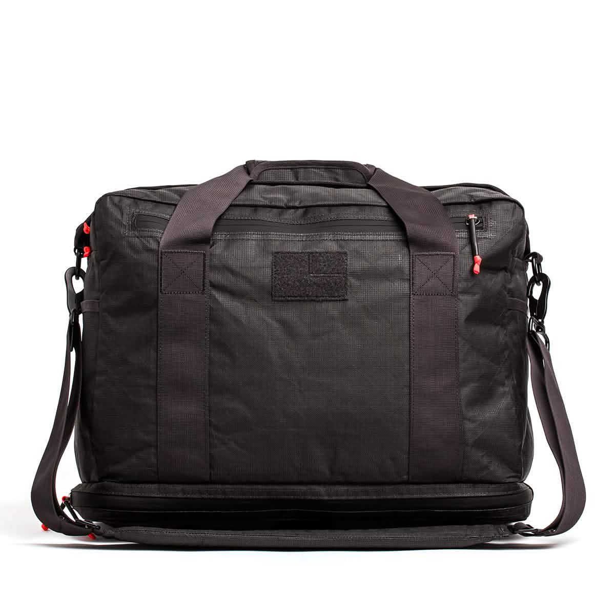The Kit Bag x Carryology - Ultra Blaze is a black duffel with sturdy handles, red zipper accents, and a shoulder strap. Made from UHMWPE fabric, it features a shoe compartment and appears against a white background.