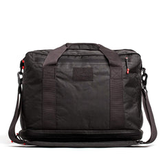 The Kit Bag x Carryology - Ultra Blaze is a black duffel with sturdy handles, red zipper accents, and a shoulder strap. Made from UHMWPE fabric, it features a shoe compartment and appears against a white background.