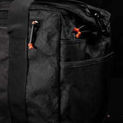 Close-up of the Kit Bag x Carryology - Ultra Blaze duffel, crafted from UHMWPE fabric, with black zippers and orange zipper pulls, set against a dark background.