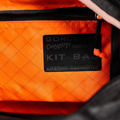 Close-up of the orange Kit Bag x Carryology - Ultra Blaze interior with a black patch labeled "GORUCK Carryology KIT BAG Lifetime Guarantee.