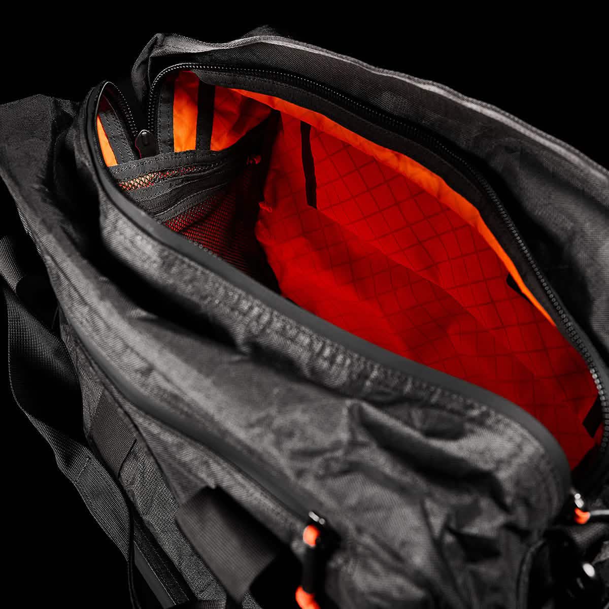 The Kit Bag x Carryology - Ultra Blaze features an open zipper showing a vibrant orange interior, mesh pocket, and shoe compartment—all crafted from durable UHMWPE fabric.
