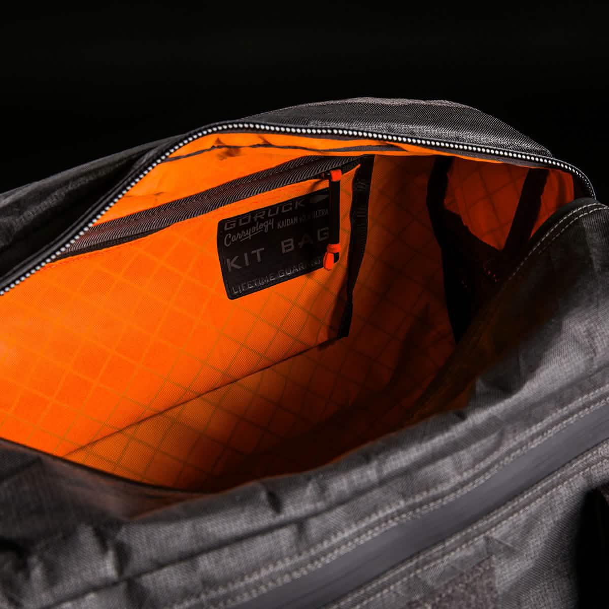 Open Kit Bag x Carryology - Ultra Blaze, featuring a bright orange interior, labeled pocket, and durable UHMWPE fabric, displayed against a dark background.