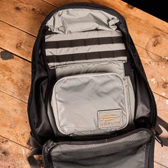 A Shadow Pockets - Ripstop ROBIC® backpack from GORUCK rests open on a wooden surface, displaying its gray storage compartment made of durable ROBIC® Ripstop Nylon and featuring a patch label inside. This lightweight storage solution includes a mesh pocket and black straps for optimal rucksack organization.
