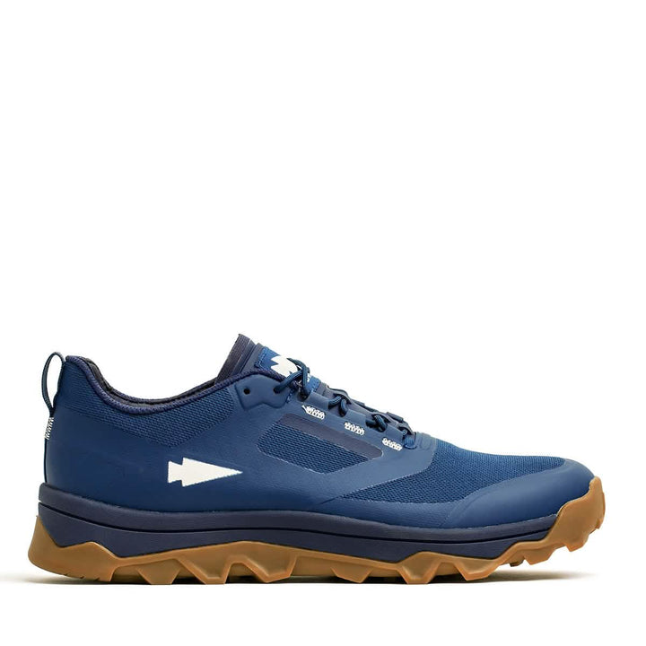 The Mackall - Legion Blue + Gum by GORUCK is a trail running shoe featuring a white arrow design on the side and a rugged brown sole for traction. Ideal for Special Forces training, it is built to conquer any terrain. Displayed against a white background, the shoe showcases its athletic style and suitability for outdoor adventures.