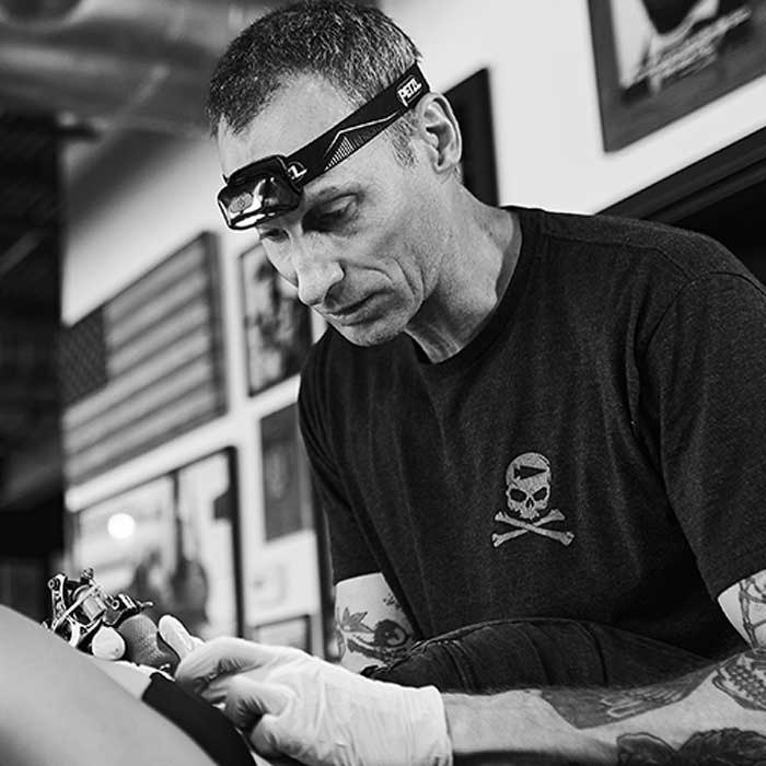 Tattoo artist wearing gloves and headlamp focuses on tattooing a client in a studio.