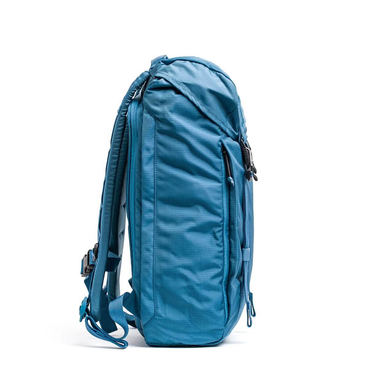 Side view of the GORUCK M23 - Ripstop ROBIC® in Tidal Blue with Speed Tan accents, showcasing its multiple zippered compartments and adjustable straps, placed against a plain white background.