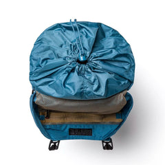 A tidal blue rucksack with its lid open reveals a drawstring closure and mesh pocket. The interior features a speed tan compartment for organization. The brand GORUCK is visible at the bottom, adding a rugged touch reminiscent of a vintage M1945 field pack.
