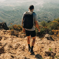 Hiker with GORUCK backpack trekking rocky mountain trail overlooking green valley