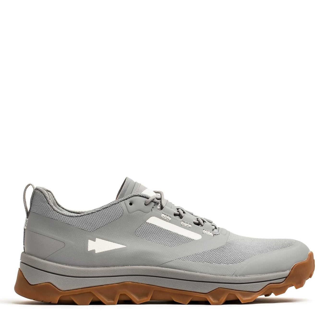 The Mackall - Chiseled Stone + Gum by GORUCK is a rucking shoe in gray with a rugged, textured sole and a white arrow logo on the side, all set against a plain white background. Its brown triple compound outsole provides outstanding contrast and grip, making it ideal for any trail adventure.