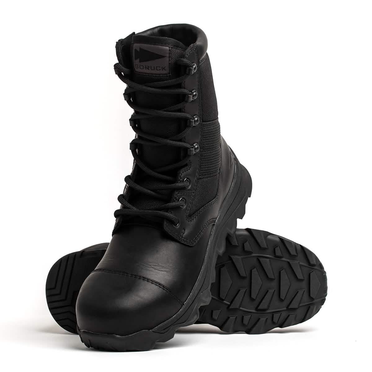 The MACV-2 Safety Boot - High Top, crafted by GORUCK to meet Special Forces standards, features rugged soles. One boot stands upright, while the other lies on its side, showcasing the thick tread pattern. The brand logo is visible on the tongue against a plain white background.