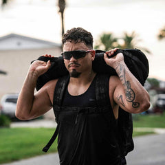 Athletic man wearing black performance tank and sunglasses carrying a heavy ruck sack outdoors