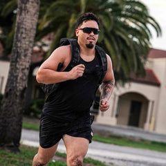 Man running outdoors wearing GORUCK black performance tank and weighted rucksack with palm trees in background