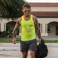 Athletic man with tattoos wearing acid lime performance tank and shorts, carrying black backpack outdoors
