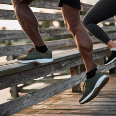 Close-up of two people wearing durable GORUCK green rucking shoes stepping on wooden steps outdoors