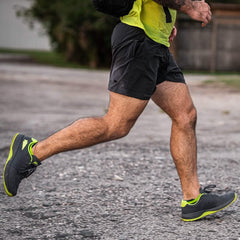 Close-up of a man running outdoors wearing black shorts, neon yellow and black athletic shoes, and a neon yellow top