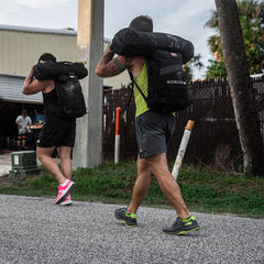 Two men carrying GORUCK rucking bags over shoulders during outdoor workout session