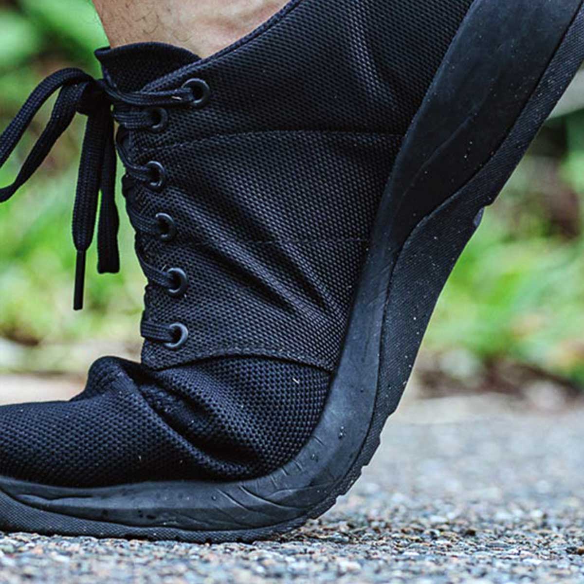 A flexible black sneaker bends as a person steps on a gravel path outdoors.
