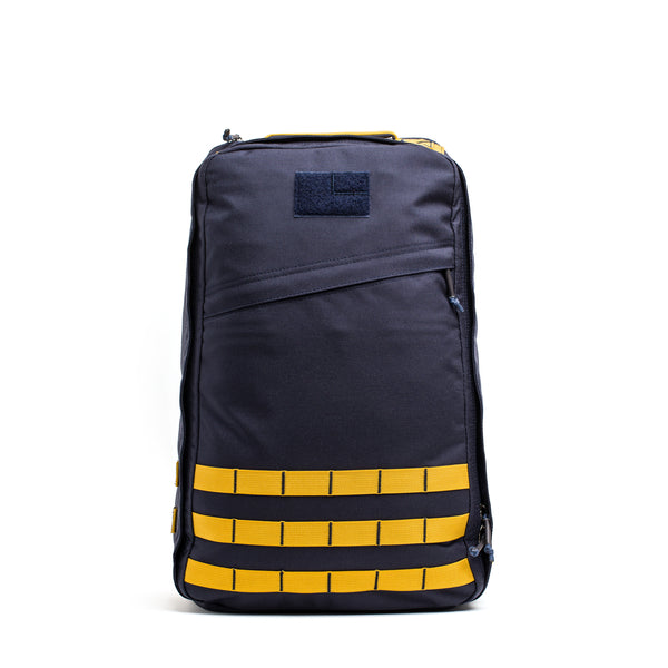 The GR1 rucksack, featuring a dark gray color with yellow horizontal straps and a front zipper pocket, is displayed against a white background.