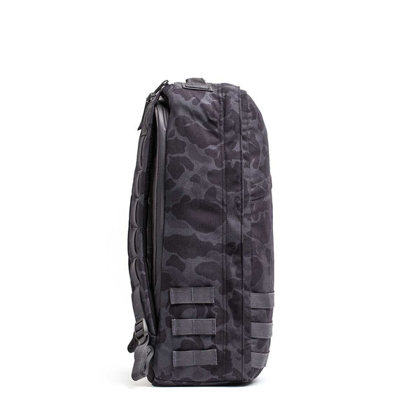 Side view of the GR1 rucksack in black and dark gray camo, featuring multiple straps and a zipper, designed to Special Forces-grade standards, shown on a white background.