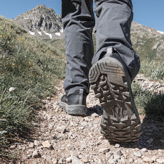 Close-up of rugged GORUCK trail shoe outsole on rocky mountain hiking path with alpine scenery