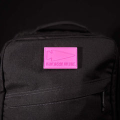 Close-up of black GORUCK backpack featuring a pink patch with embossed arrowhead logo and GORUCK text