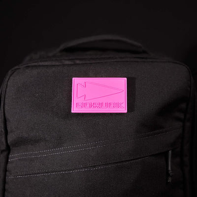 The GORUCK PVC Patch, featuring a stylized arrow design and the brand's name in bold pink on a durable black background, channels the essence of Special Forces with its striking spearhead-inspired contrast.