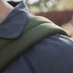 Close-up of a person wearing a dark-colored shirt with a green shoulder strap from the GORUCK Kit Bag, resting on their shoulder against a blurred outdoor background.
