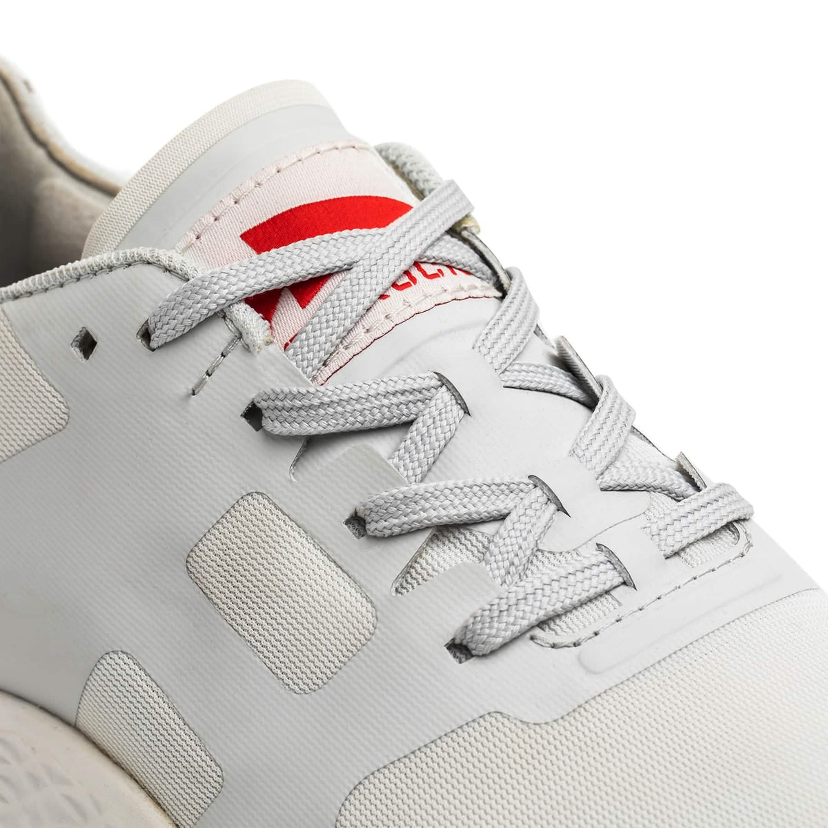 Close-up of the Men's Rough Runner - Light Grey + Red sneaker, featuring gray laces, a red tongue logo, and a lightweight design with a Gradient Density EVA midsole.