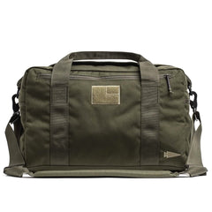 Introducing the Kit Bag (Includes Shoulder Strap) by GORUCK - a durable olive green canvas duffel crafted in the style of an Aviator’s Kit Bag. It comes with two handles, a detachable shoulder strap, and boasts a rectangular patch on the front along with a small side zipper pocket, making it perfect for versatile use and travel.