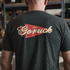 Man wearing the GORUCK Bud Tee - Tri-BlendX, featuring a bold red and gold "Goruck" logo on the back. Ideal for everyday wear and comfort indoors.