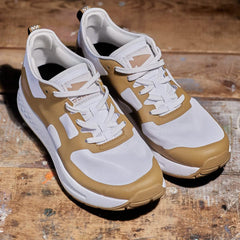 The Men's Rough Runner - Speed Tan by GORUCK is a modern pair of sneakers ideal for the Rough Runner, showcasing a sleek white and light brown color scheme against a rustic wooden backdrop. These shoes feature textured soles with gradient density for enhanced comfort and visible laces.
