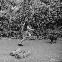 A man wearing Merino wool ankle workout socks jogs on a path toward a dog, with two sandbags lying on the ground in the foreground.