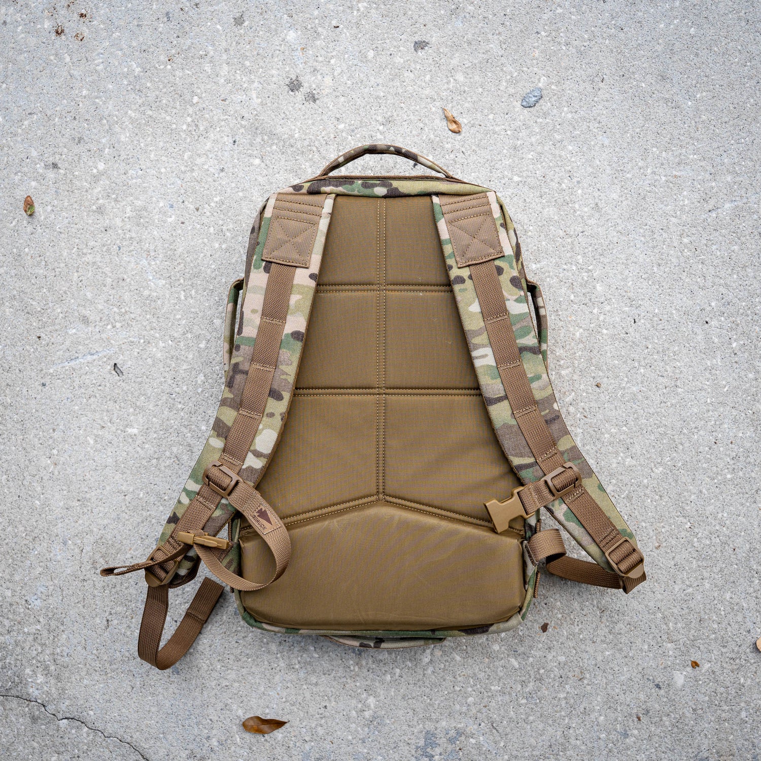 The Rucker 5.0, featuring a camouflage pattern, padded straps, and lumbar support, rests on a concrete surface.