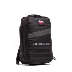 The Rucker 5.0, a black GORUCK rucksack featuring an American flag patch, MOLLE webbing, and space for ruck plates, stands upright on a white background—ideal for your next rucking challenge.