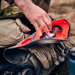 Someone puts goggles into an open Rucker 5.0 rucksack, with a dirty shoe and water bottle nearby, getting ready for a day of rucking.