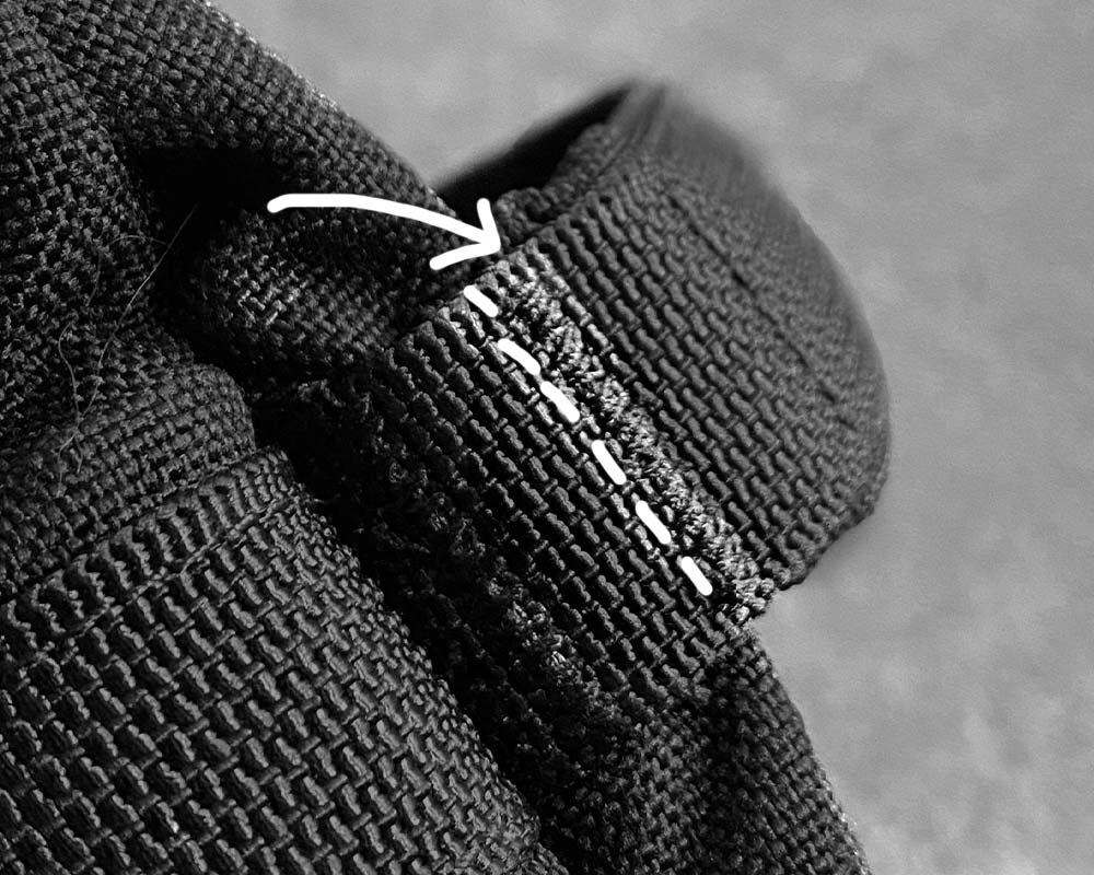Close-up of black fabric with visible stitching and a white arrow pointing at a seam.