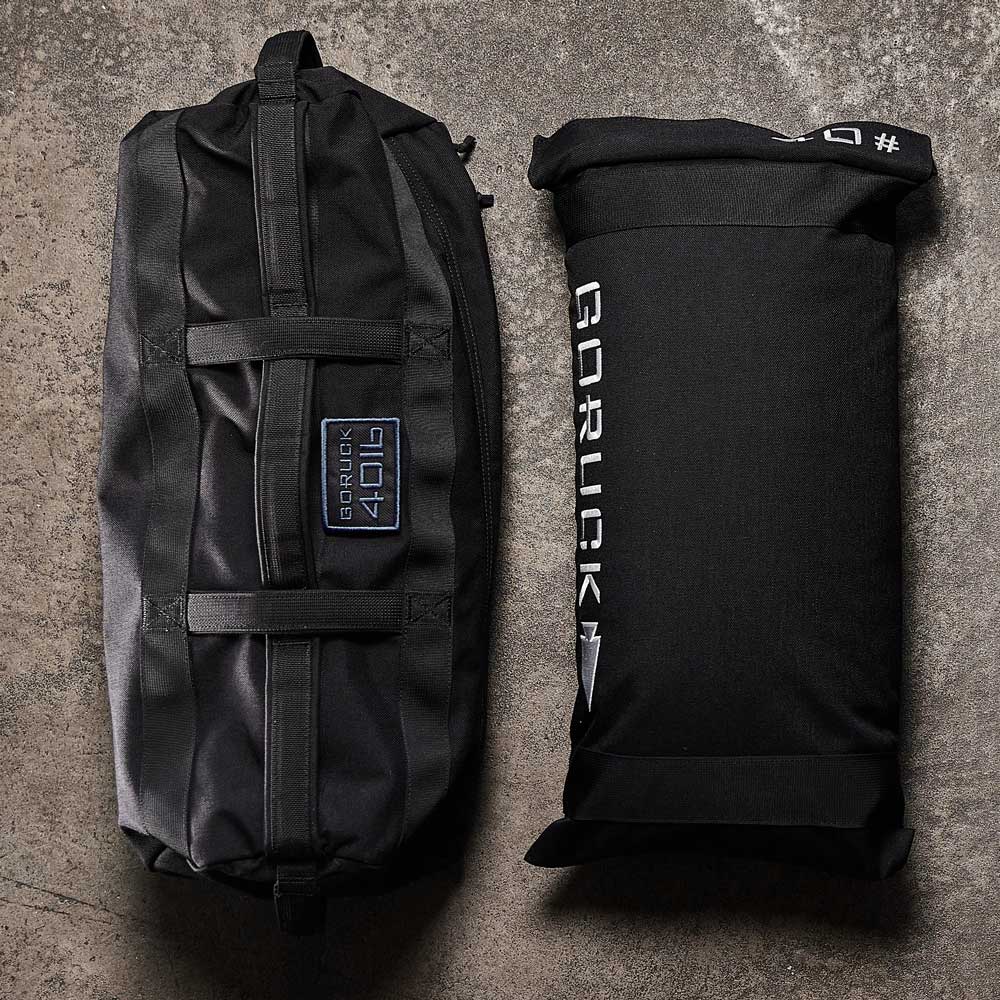 Two black GORUCK workout sandbags on a concrete floor, one lying flat and one standing upright.