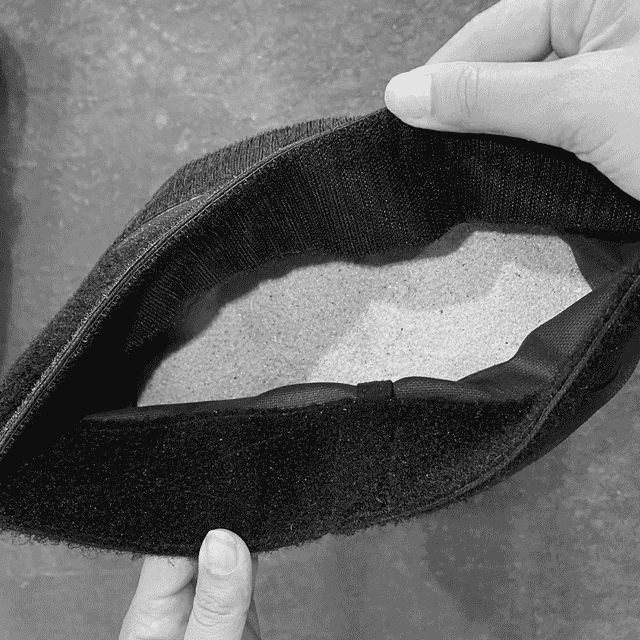 A person holds open a black pouch filled with sand, showing the pouch’s interior.