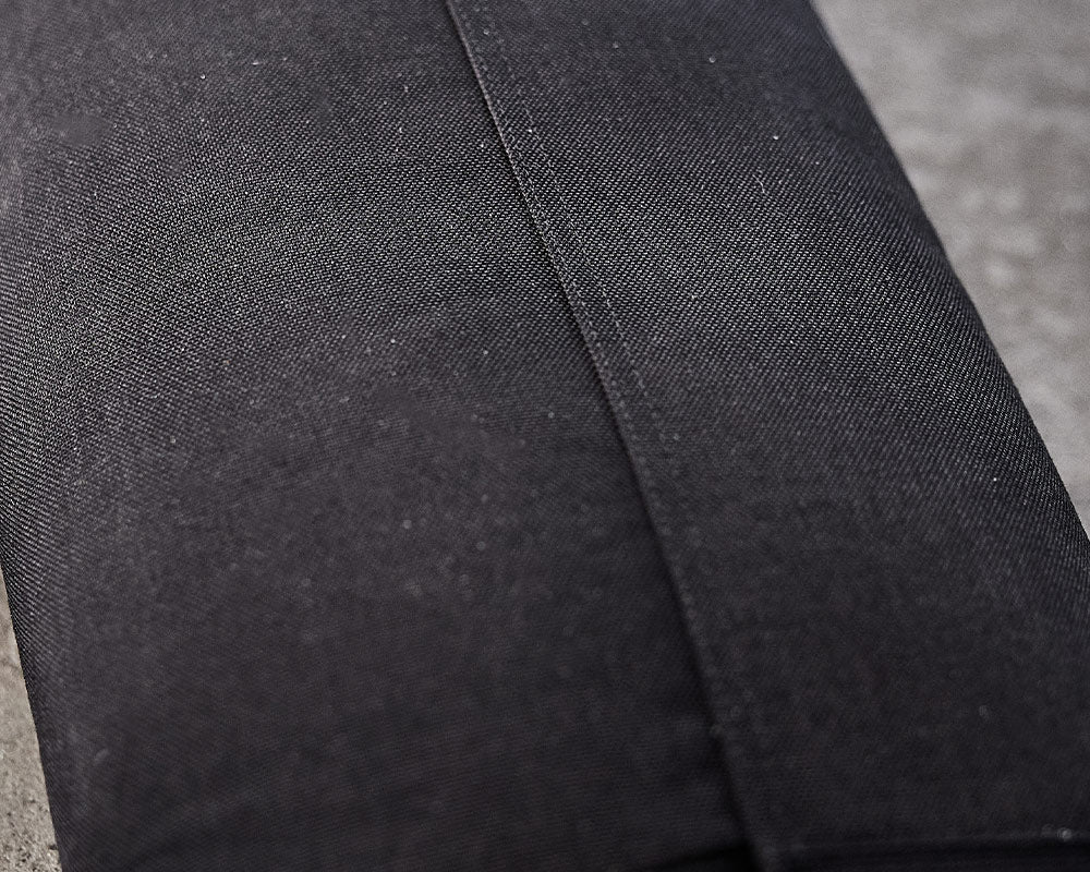 Close-up of folded black fabric with a visible seam, shown on a gray surface.