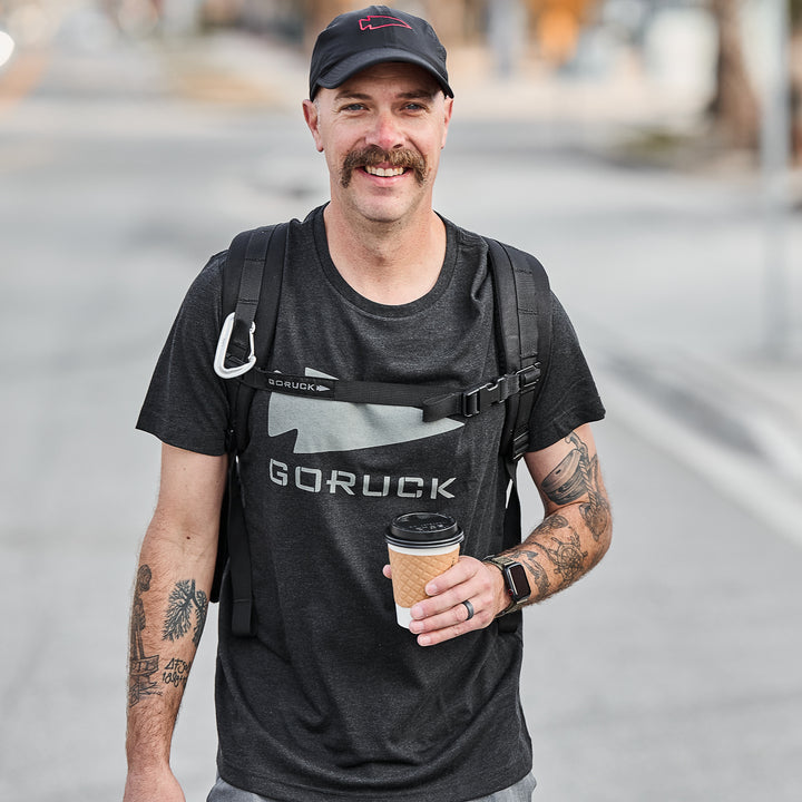 Semi-famous man with a mustache, wearing a black Three Rules Tee - Tri-Blend from GORUCK and a backpack, holding a coffee cup and smiling outdoors.
