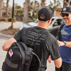 Man wearing GORUCK black The Three Rules t-shirt and cap carrying GORUCK bag shaking hands outdoors