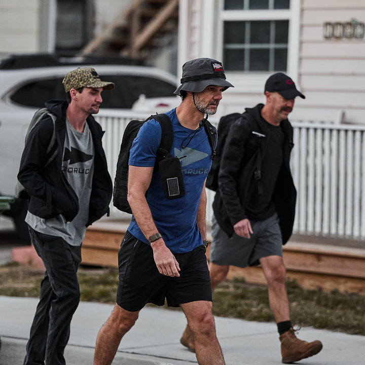 Three men wearing Three Rules Tee - Tri-Blend casual shirts and hats walk together on a sidewalk in front of a house, as if posing for candid photos.