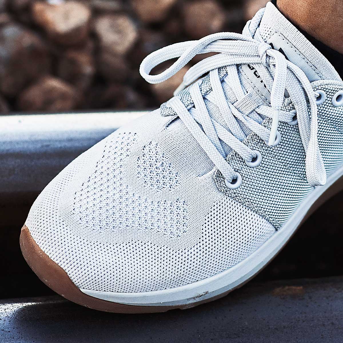 Close-up of a white athletic shoe with laces, worn by a person standing on a metal rail.