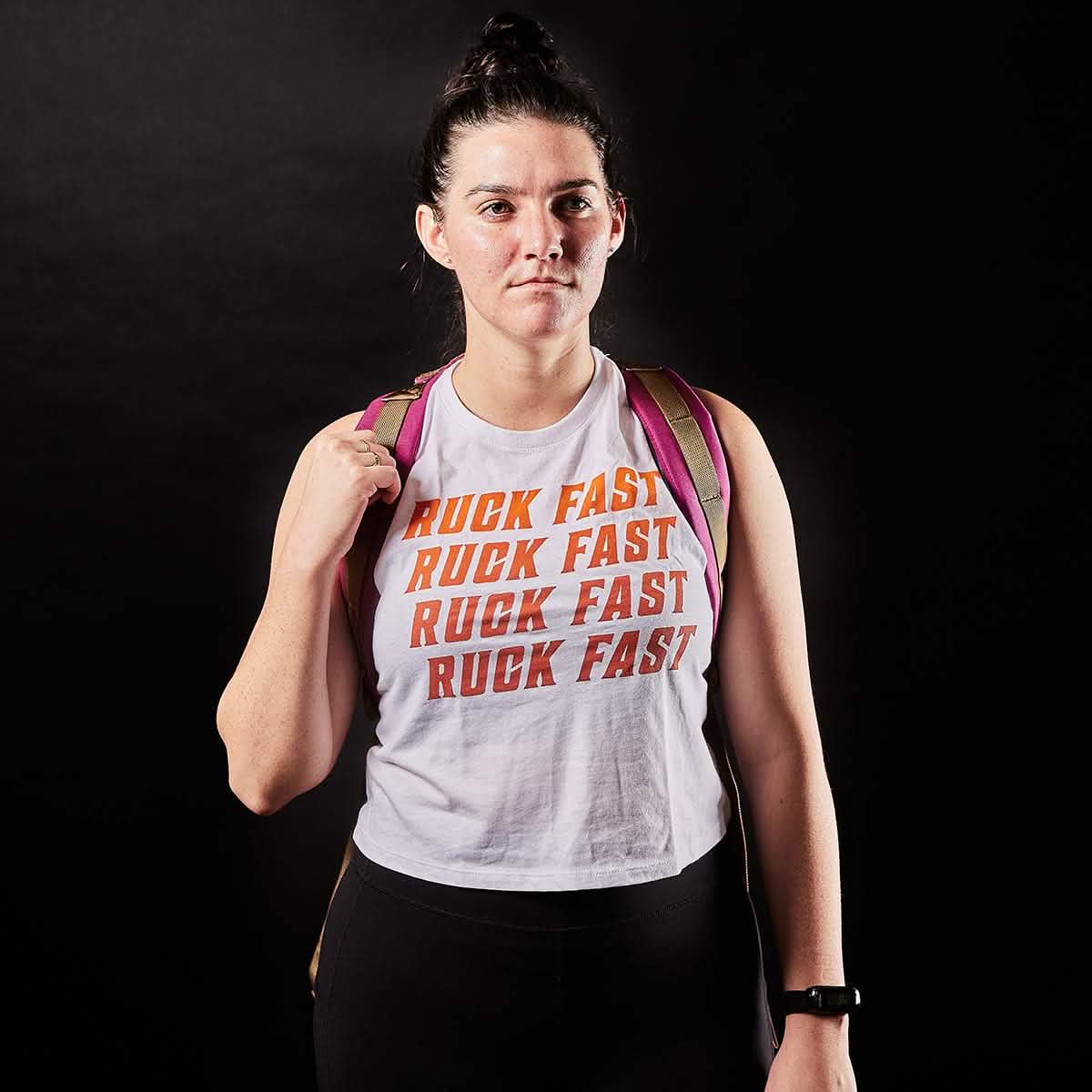 Against a dark background, an adventurous person with a bun hairstyle is confidently wearing the Women’s Ruck Fast Tank - Tri-Blend by vendor-unknown. The tank features bold orange 
