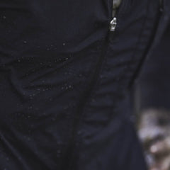 Close-up of a black Indestructible Challenge Windbreaker with a zipper, lightly speckled with water droplets, crafted from abrasion-resistant ToughDry fabric.