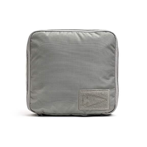 The GORUCK Shadow Pockets - Ripstop ROBIC® is a square gray fabric pouch crafted from robust RIPSTOP ROBIC Nylon. It showcases a minimalist arrow-shaped design patch on the front, making it ideal for storing lightweight gear. The textured accessory also features visible stitching along the edges to enhance organization within your rucksack.