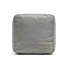 The GORUCK Shadow Pockets - Ripstop ROBIC® is a square gray fabric pouch crafted from robust RIPSTOP ROBIC Nylon. It showcases a minimalist arrow-shaped design patch on the front, making it ideal for storing lightweight gear. The textured accessory also features visible stitching along the edges to enhance organization within your rucksack.