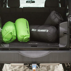 Three Sea to Summit sleeping bags rolled and packed inside the open trunk of an off-road vehicle on a sandy terrain