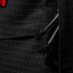 Close-up of a black textured Japanese cotton fabric bag with two black zipper pulls and part of a red label visible, from the exclusive GR1 USA x Carryology - GRXC2 Samurai collection.